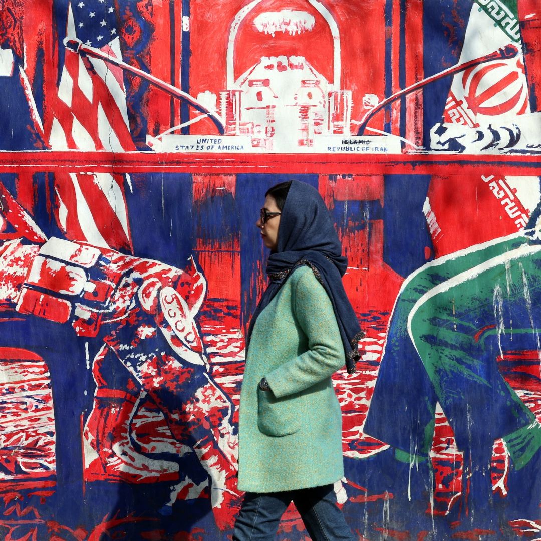 An Iranian woman walks past a mural depicting Iran and the United States at the negotiation table, painted on the outer walls of the former U.S. embassy in Tehran, on Feb. 6, 2026.