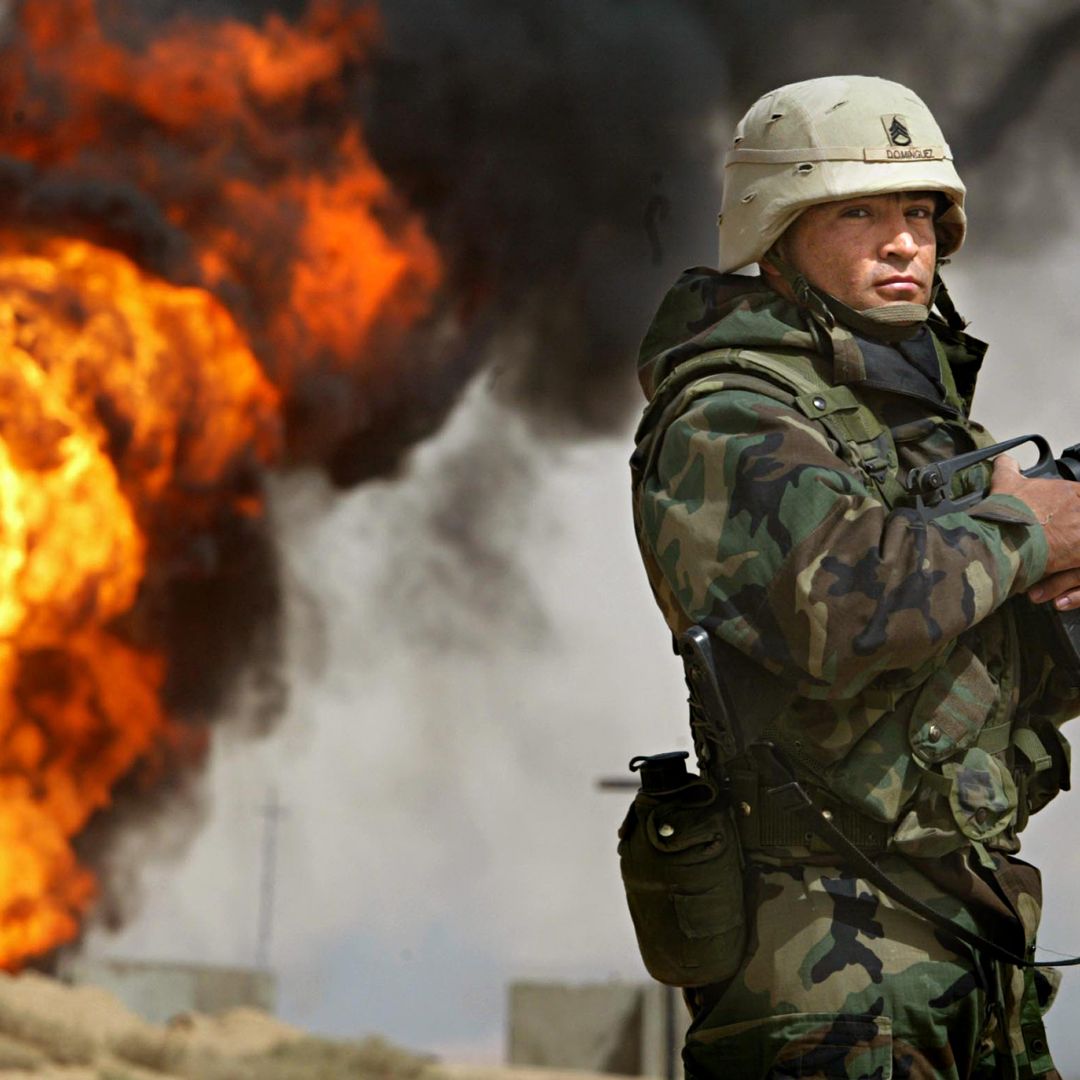 U.S. Army Staff Sgt. Robert Dominguez stands guard next to a burning oil well in the oil fields of Rumaila, Iraq, on March 27, 2003.