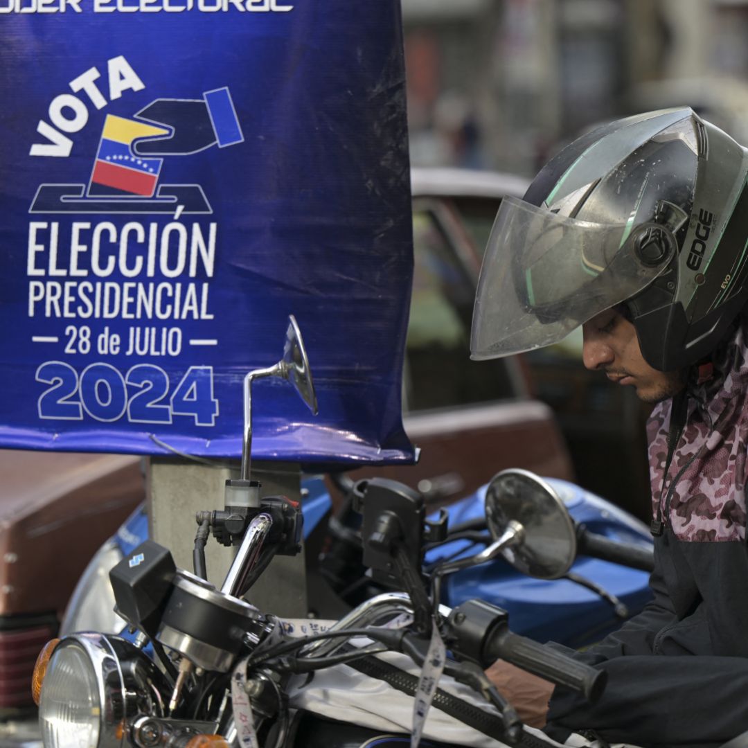 A motorcyclist looks at his phone in front of a National Electoral Council poster promoting the upcoming presidential election in Caracas, Venezuela, on July 23, 2024.