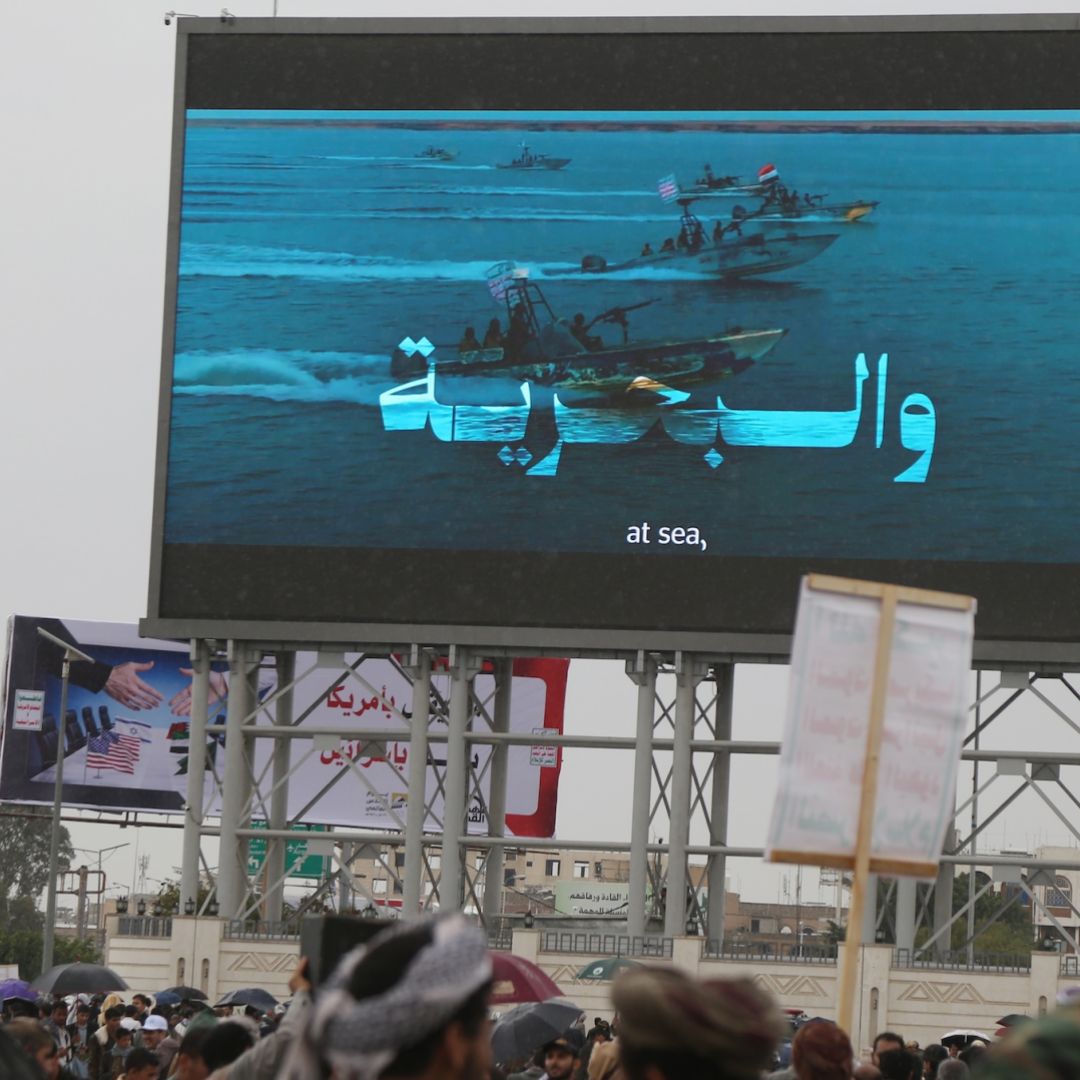 People in Sanaa, Yemen, stand under a large screen broadcasting Houthi-run coastguard forces patrolling in the Red Sea on March 13, 2026.