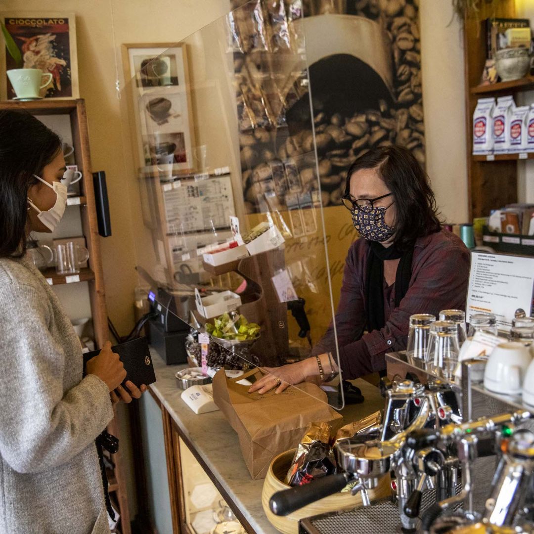 A shopkeeper wearing a protective mask serves a client on April 22, 2020, in Berlin from behind a protective plastic screen in a coffee store open for the first time since a COVID-19 shutdown.