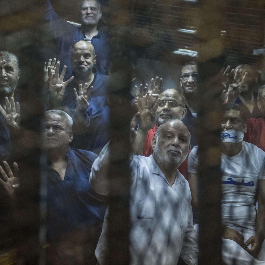 Egyptian Muslim Brotherhood senior members, including Khairat al-Shater (top left), gesture from the defendants' cage at the Egyptian Police Academy on the outskirts of Cairo on June 2, 2015. 
