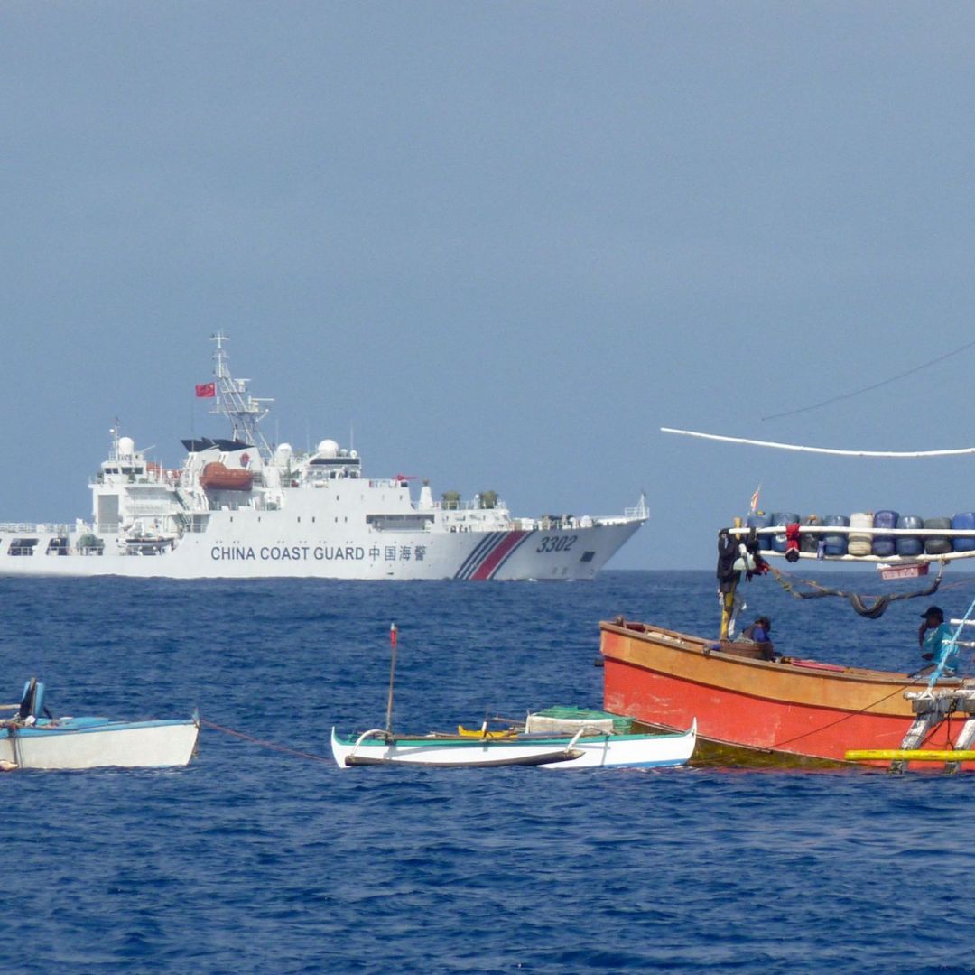 A Chinese coast guard ship sails past anchored Philippine fishing boats in the Scarborough Shoal, in the disputed South China Sea, on Feb. 3, 2023.