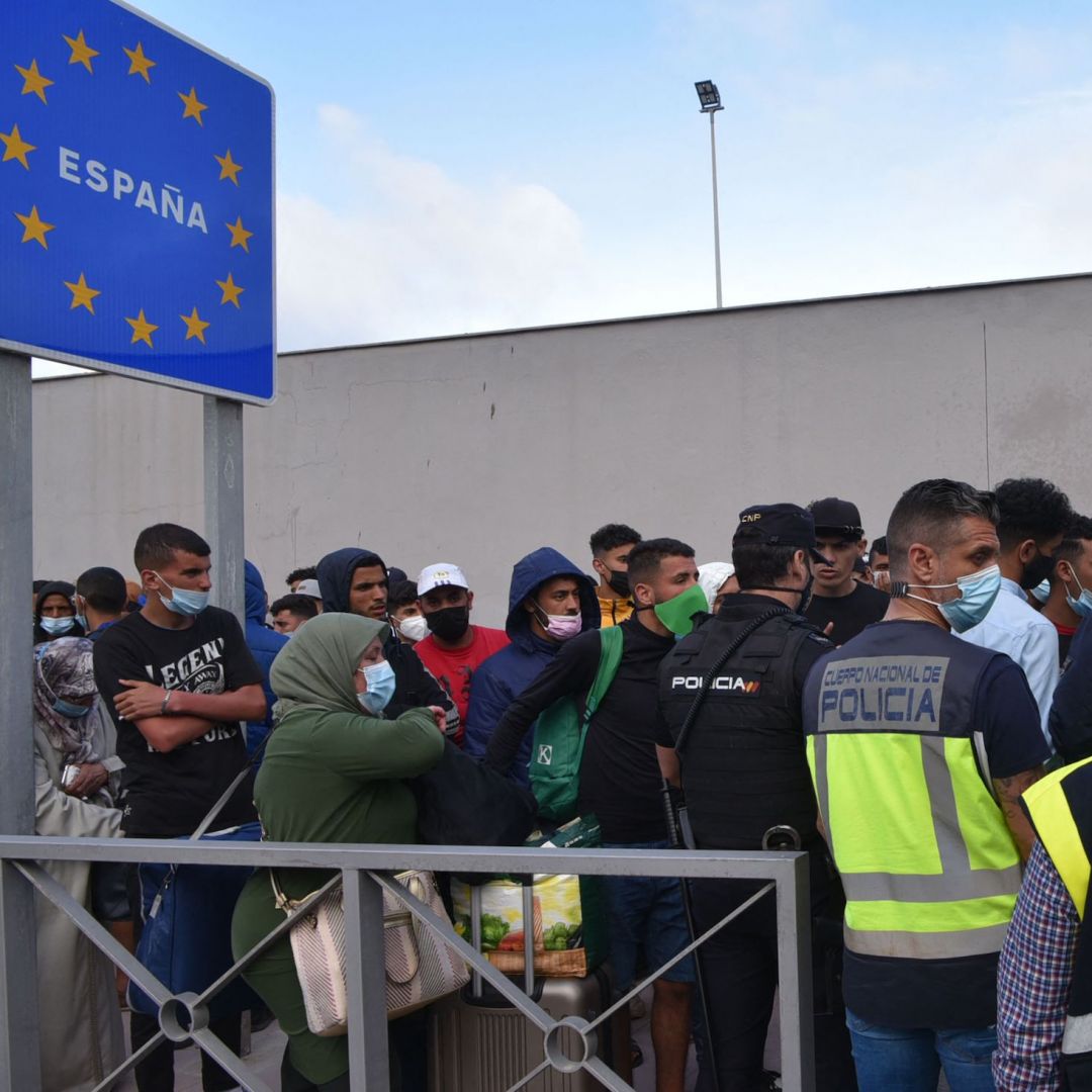 Spanish policemen stand next to migrants waiting to cross the border back to Morocco at the Spanish enclave of Ceuta on May 20, 2021. Spanish policemen stand next to migrants waiting to cross the border back to Morocco at the Spanish enclave of Ceuta on May 20, 2021.