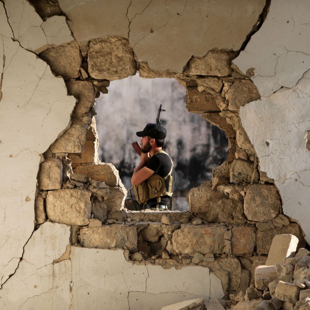 A fighter of the Turkish-backed Syrian National Army is seen through the hole of a damaged building in the northern town of Marea, facing the Kurdish-controlled area of Tal Rifaat, on Aug. 2, 2022. 