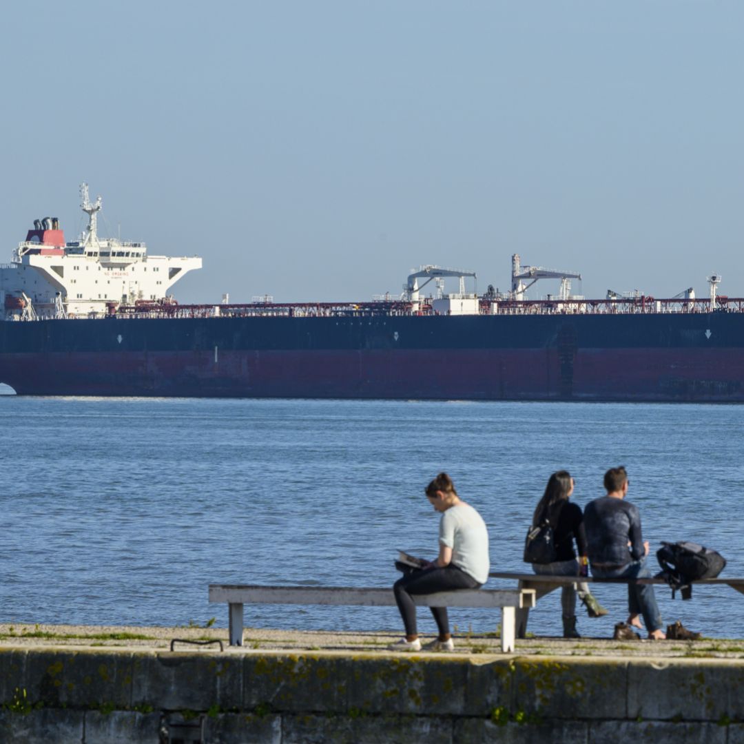 People relax on the bank of the Tagus River where Venezuelan PDVSA oil tanker Rio Arauca lies at anchor, having been impounded by Portuguese authorities for nearly two years due to unpaid debt, March 9.  