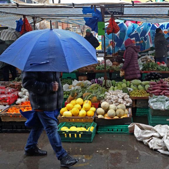 A pedestrian shelters from the rain as they walk past fruit and vegetables displayed for sale at a market in east London on March 31, 2023.
