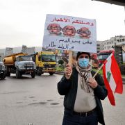 A protester holds a sign as fuel tankers block a road in Lebanon's capital of Beirut during a general strike by public transport and workers unions on Jan. 13, 2022. A protester holds a sign as fuel tankers block a road in Lebanon's capital of Beirut during a general strike by public transport and workers unions on Jan. 13, 2022.